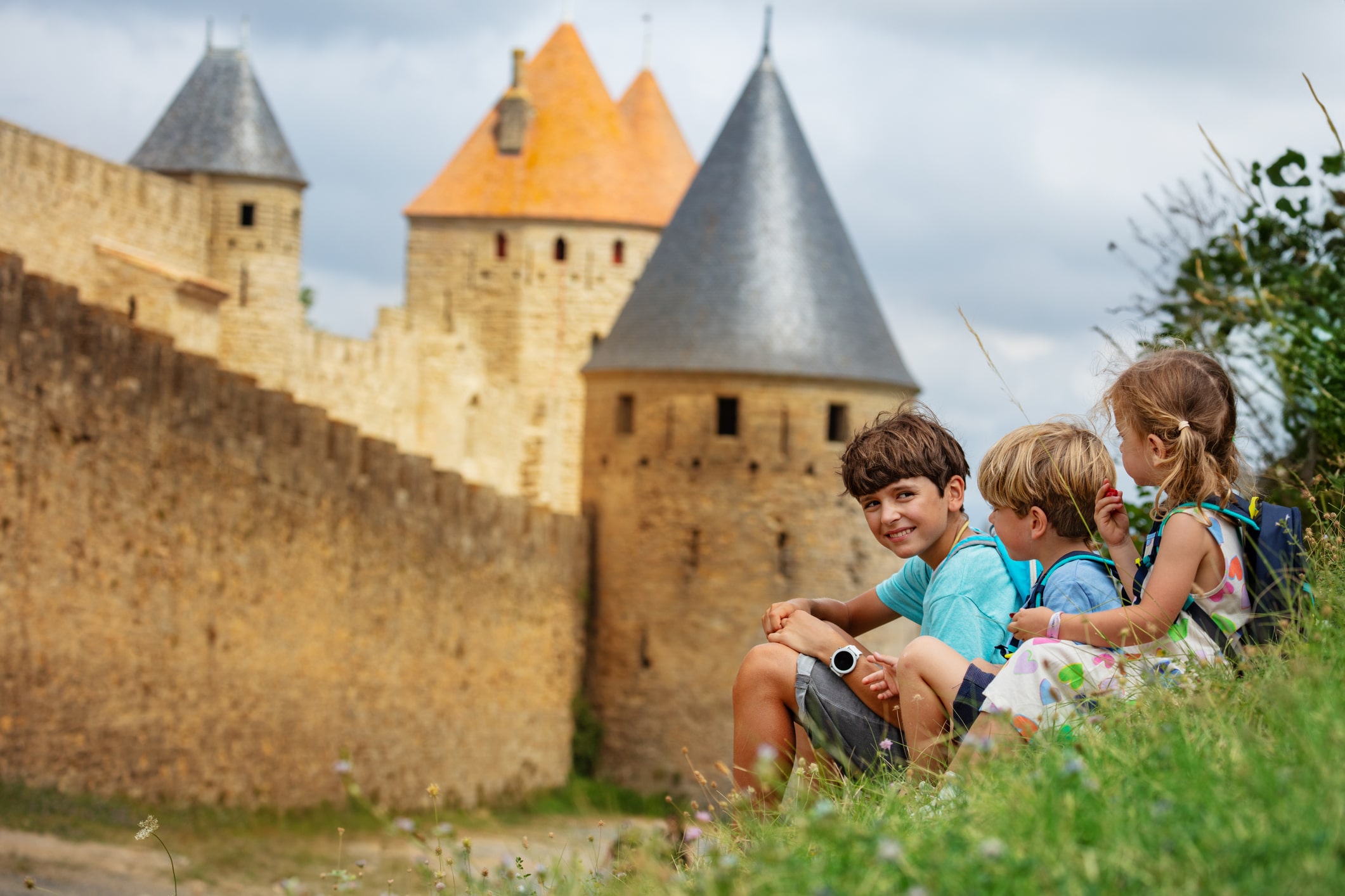 Kids resting on the grass below the medieval castle walls and towers of Carcassonne