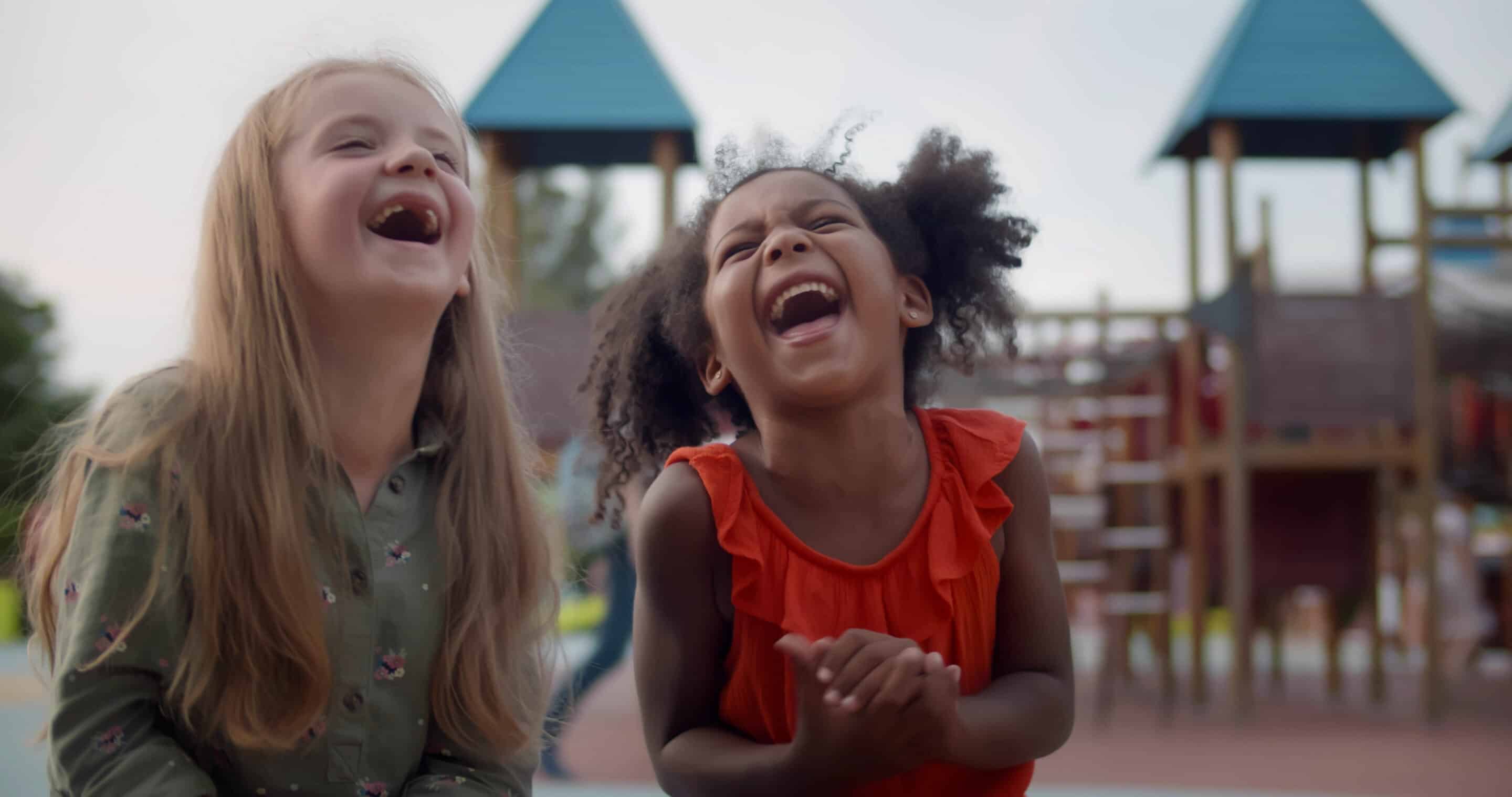 Two little girls laughing together on a bench at a playground