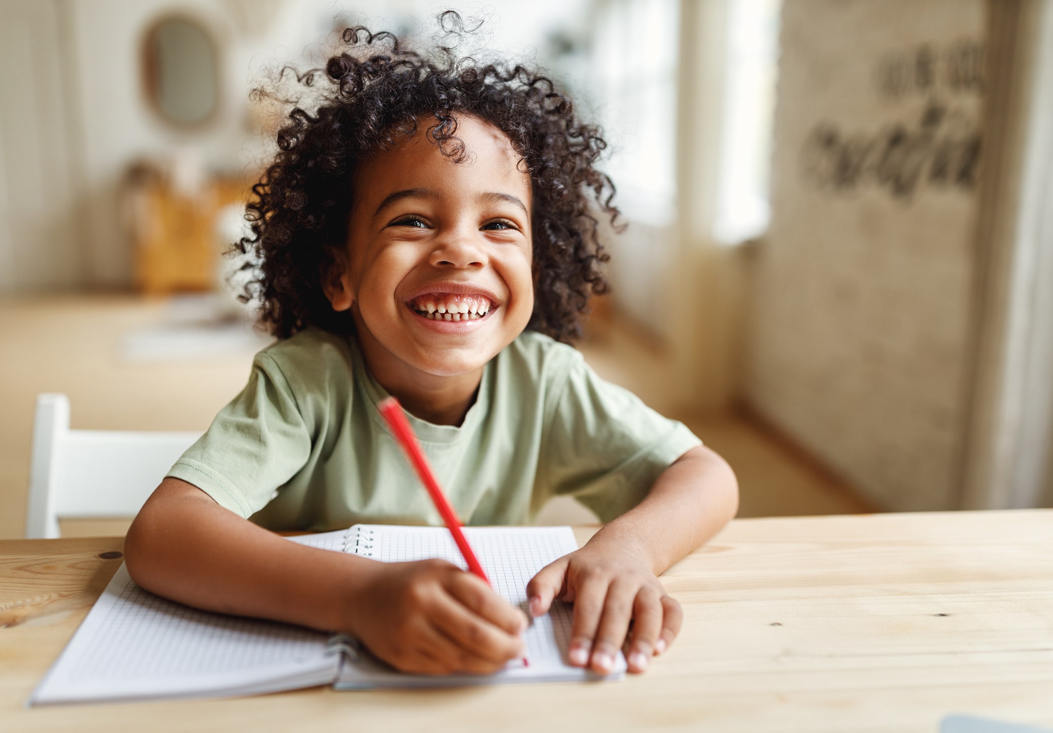 Smiling boy writing in a notebook at a table at home