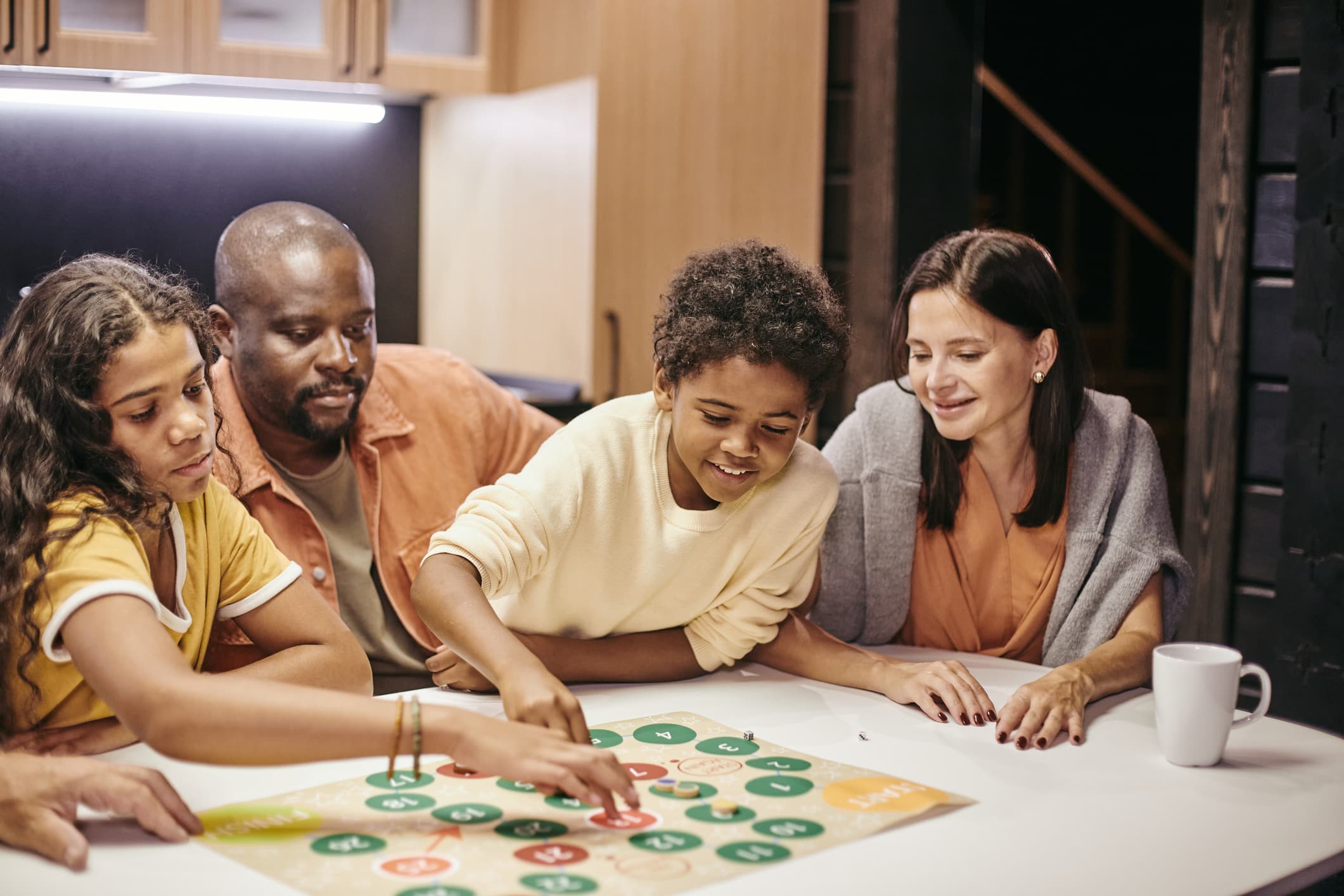 Family laughing around a kitchen table while playing a board game together