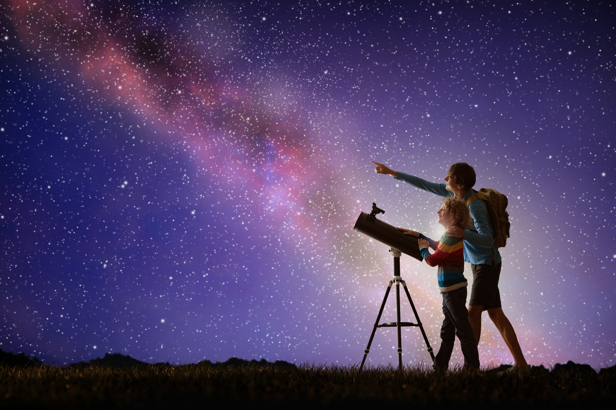 Parent and child pointing a telescope at the Milky Way on a starry night