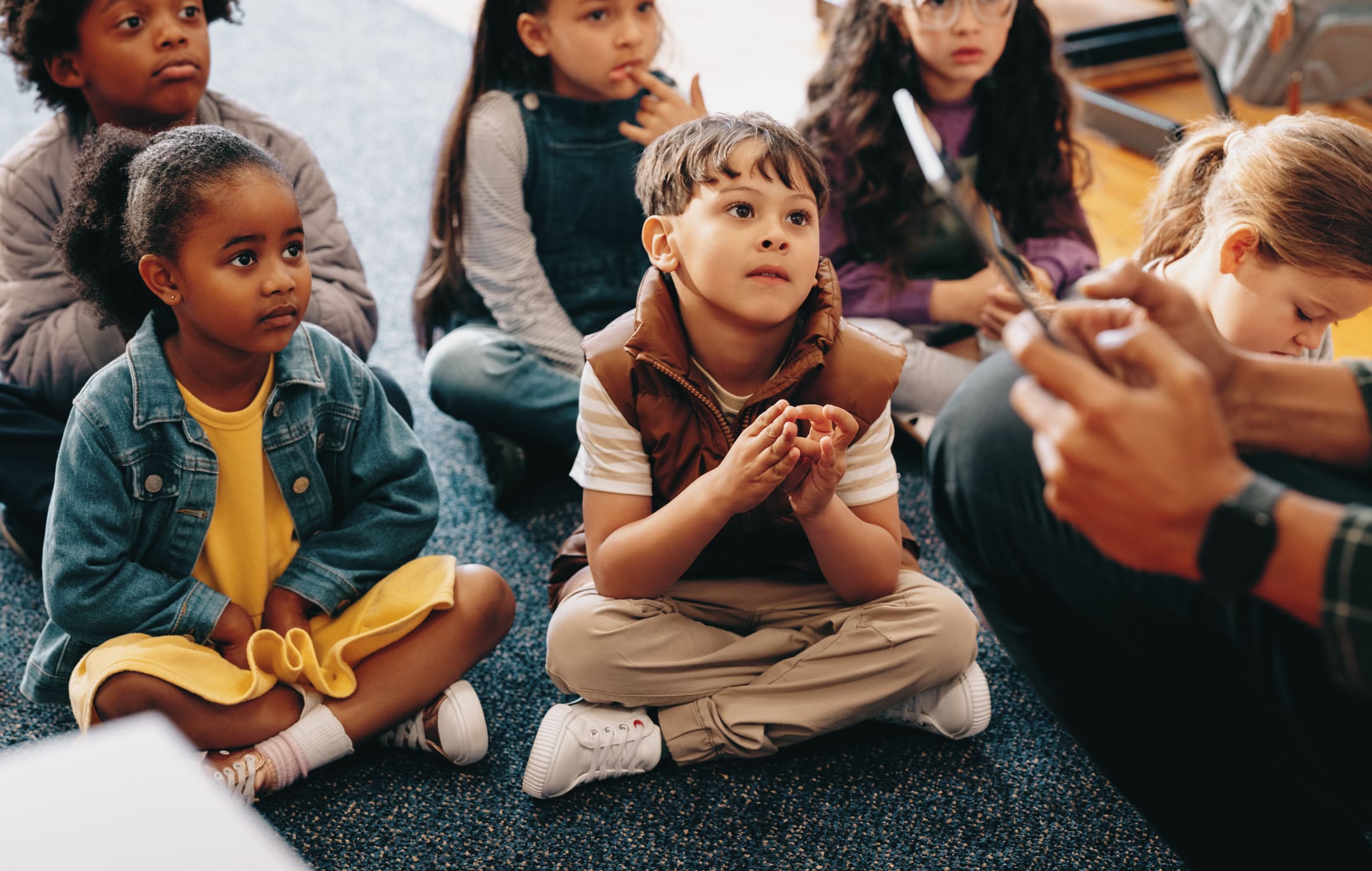Elementary students sitting on a classroom carpet listening to their teacher