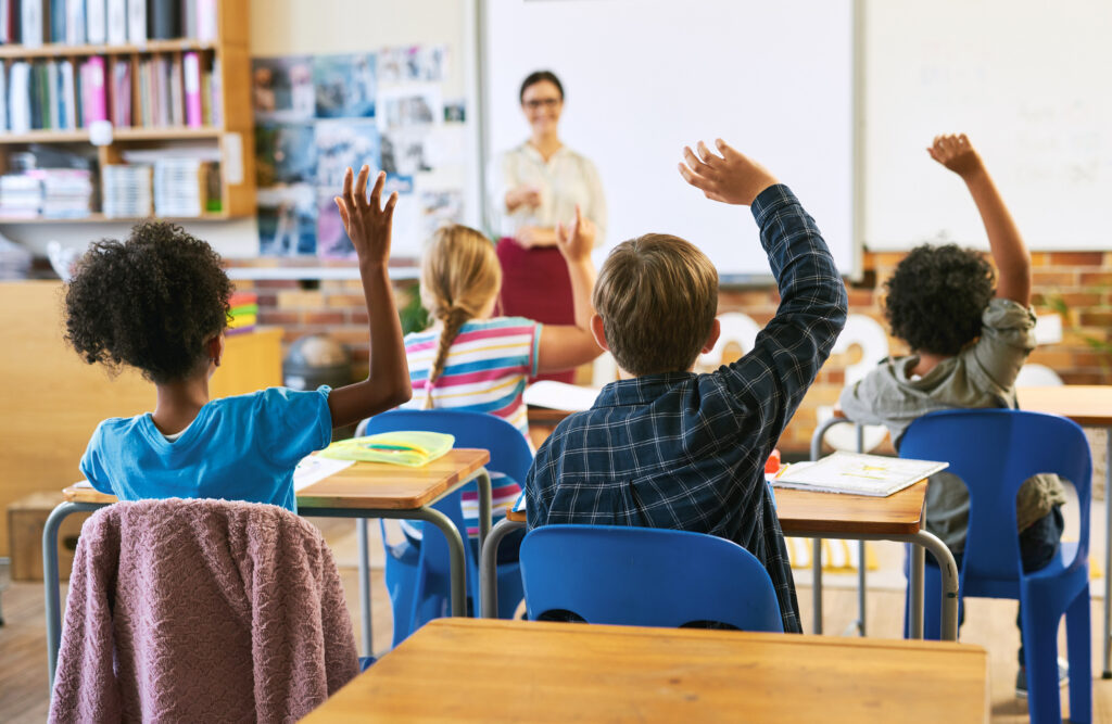 Elementary students raising their hands to answer a question in class
